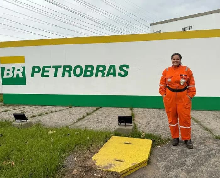 Imagem de egressa do Programa Autonomia e Renda Petrobras no IFSP com traje de trabalho em frente a uma unidade da Petrobras.