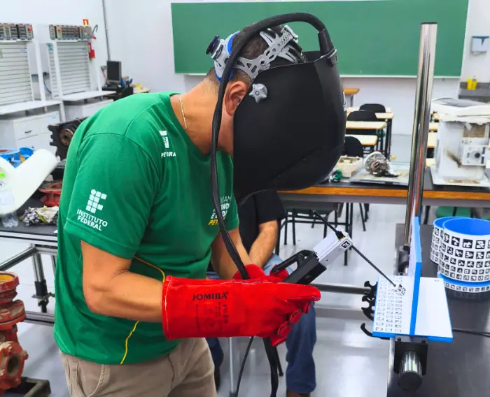 Imagem de estudante do curso de Soldador do IFPR com capacete de solda em aula prática.
