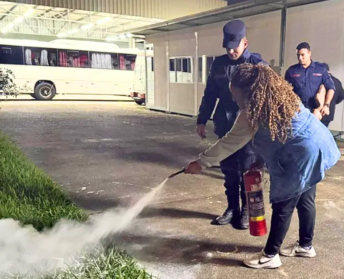 Imagem de uma estudante do Programa manuseando um extintor de incêndio, sob supervisão de bombeiros.
